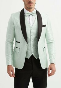 Veste de smoking vert menthe clair en tissu texturé, avec revers en satin noir, gilet assorti et nœud papillon. Présente des accents de poche noirs.