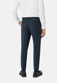 Celana slim-fit berwarna navy dengan tekstur halus, bagian depan datar, dan dua saku belakang. Dipadu padankan dengan sepatu hitam dan kemeja lengan panjang putih.