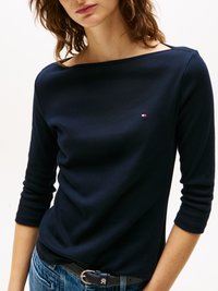 Marineblå langermet topp med båtistrikking og ribbestruktur, med en liten logo brodert på brystet. Båret sammen med klassiske blå jeans.