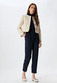 Beige lyhytrakuläinen takki nappien kanssa, tummansiniset korkeavyötäröiset housut ja kermaiset ballerinat. Sileä pinta, istuva leikkaus ja minimalistinen muotoilu.
