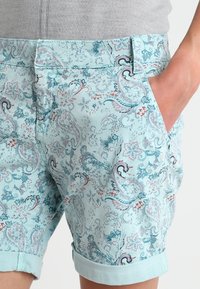 Jasnoniebieskie szorty w wzory z motywem paisley w odcieniach teal, różowym i ciemnoniebieskim, z podwiniętymi mankietami i bocznymi kieszeniami.