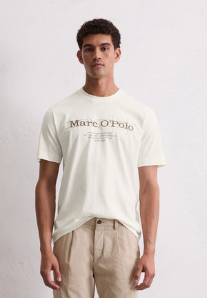 Off-white t-shirt met korte mouwen en ronde hals, voorzien van bruine tekstgraphics en een ontspannen pasvorm, gecombineerd met beige broeken.
