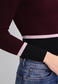 Burgundin värinen ribbipaita, jossa musta ja vaaleanpunainen raidallinen vyötärökaistale. Ominaisuuksiin kuuluu pitkät hihat ja slim fit -muotoilu.