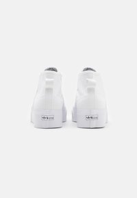 Pair of white high-top sneakers with raised platform soles and pull tabs, viewed from the back on a plain white background.