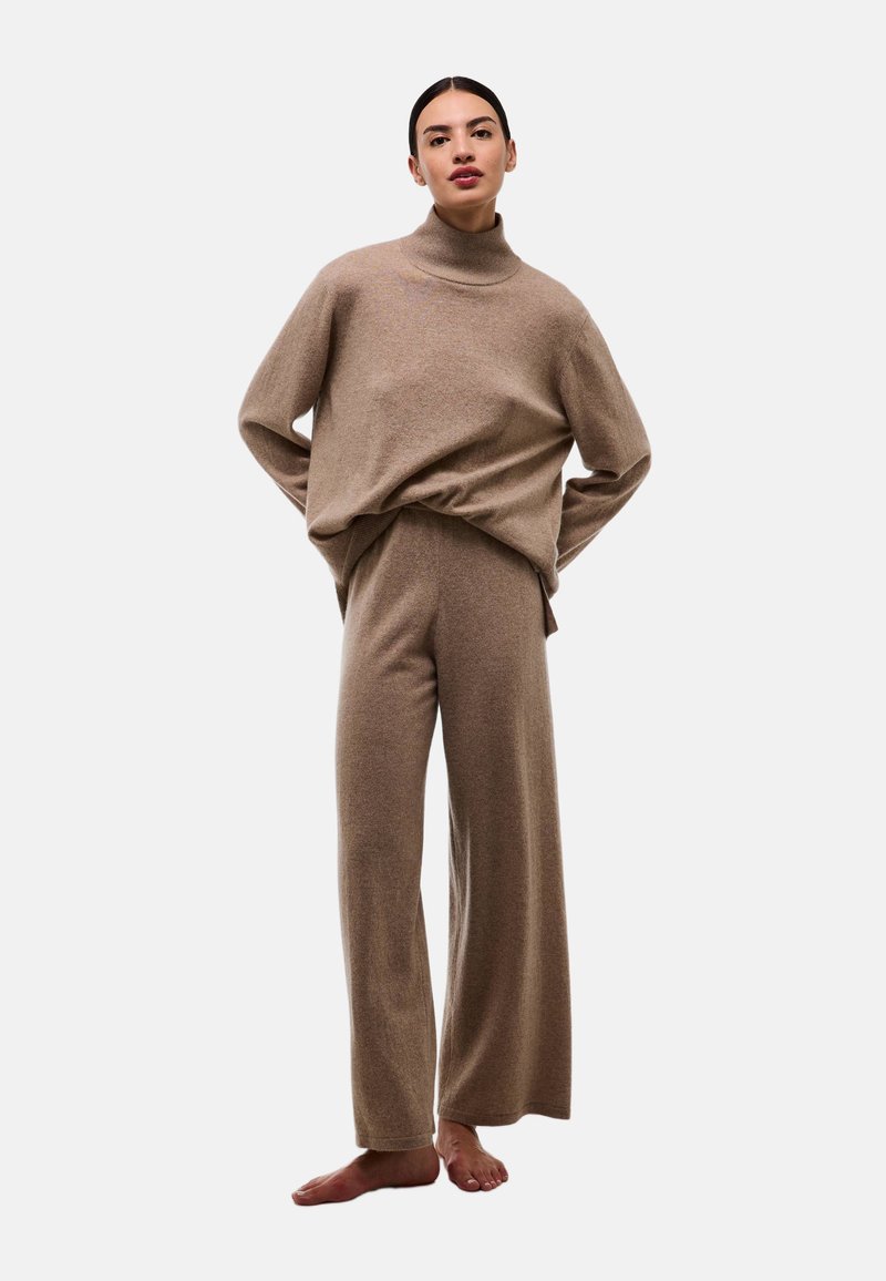 Pull en maille beige avec un col haut, associé à un pantalon large en même matière. Texture lisse, coupe décontractée, style casual.