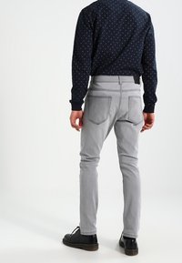 Jeans grigi slim-fit con vita piatta e cinque tasche, visti da dietro. Sono visibili anche scarpe nere e una camicia a fantasia blu navy.