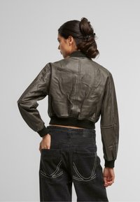 Lühenud, oliivroheline nahkbumi jakk koos soonilise krae ja mansettidega. Tumedad teksapüksid, millel on eristuv valge õmblus tagakottidel.