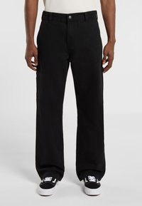 Pantalones de pierna ancha negros hechos de algodón con cierre de botón, que cuentan con bolsillos laterales y un diseño limpio. Combinados con zapatillas negras y blancas.
