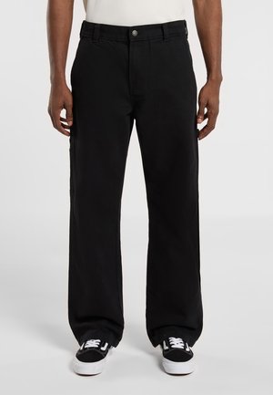Black wide-leg pants made of cotton with a button closure, featuring side pockets and a clean design. Worn with black and white sneakers.