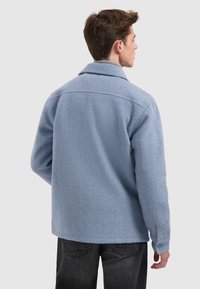 Lichtblauwe wollen jas met een kraag, knoopmanchetten en een gestructureerde afwerking. De achterkant heeft een naaddetail en een iets losser fit.
