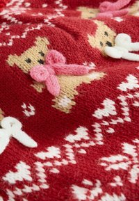 Red knitted fabric featuring teddy bears with pink bows, white accents, and geometric patterns, creating a playful design.
