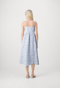 Robe florale bleue avec des bretelles fines, taille cintrée et jupe fluide qui tombe en dessous du genou. Le tissu a une texture douce et un léger motif.