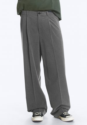 Pantalon large à rayures grises porté avec des baskets noires et blanches, associé à un haut vert foncé raccourci au-dessus de la taille.