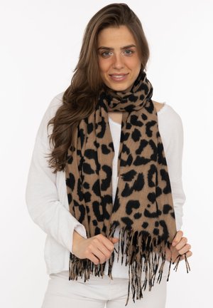 Young woman with long brown hair wearing a white sweater and a brown and black leopard print fringed scarf.