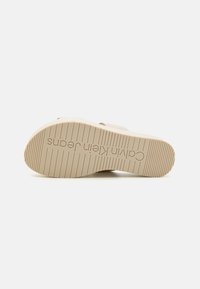 Suola di scarpa in gomma beige con scanalature orizzontali e marchio Calvin Klein Jeans. Forma arrotondata con una base piatta per maggiore stabilità.