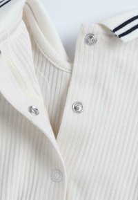 Gros plan sur un tissu à rayures blanches avec une fermeture à bouton-pression et une partie d'un col comportant des rayures noires.