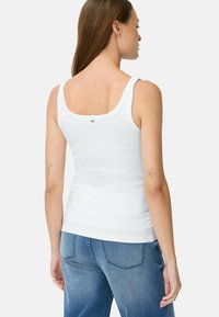 Weißes Tanktop aus Baumwolle mit breiten Trägern und runder Rückenpartie. Der Stoff ist glatt und figurbetont, mit einem kleinen Logo-Detail am Ausschnitt.
