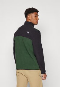 Mustmust ja rohelise värvi fliisk Jacket kõrge kaelusega, mille seljal on The North Face logo, tekstureeritud kangas ja mugav lõige.
