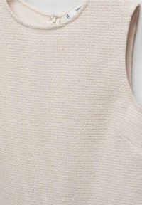 Kermantri kermava tuarimokku ilmanhihojen kanssa, jossa on pyöreä kaula-aukko ja pieni napitus takana kaulalla.