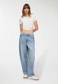 Biały krótki t-shirt z krótkimi rękawami, połączony z luźnymi, jasnoniebieskimi dżinsami. Dżinsy mają niewielkie przetarcia i tradycyjny pięcio kieszeniowy kroj.