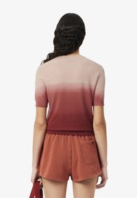 Camiseta de punto de manga corta con degradado que va de rosa claro a rojo intenso, combinada con pantalones cortos rojos a juego que cuentan con un bolsillo trasero.