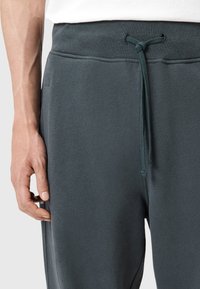 Donkergrijze sweatpants gemaakt van zachte stof, met een tailleband met trekkoord en zijzakken. De textuur lijkt glad met een subtiele glans.