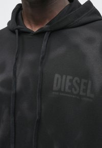 Melns džemperis ar kapuci, priekšējo kabatu, auklām un nelielu "DIESEL" logotipu uz krūtīm. Izgatavots no gludas, teksturētas auduma.