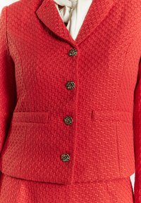 Roter strukturierter Blazer mit einem subtilen Rautenmuster. Verfügt über einen Reverskragen, vier dekorative Knöpfe und zwei Vordertaschen.