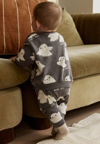 Halli puuvillane väikelapse komplekt, millel on valged kummitusmustrid oranžide põskedega, soonikkoes mansetid ja vöökoht, koos beežide sokkidega.