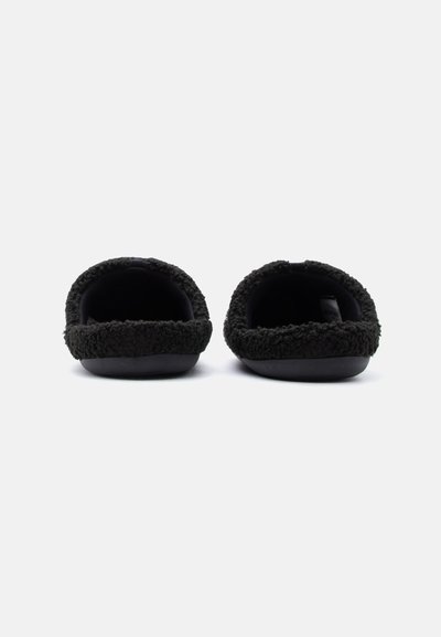 Chaussons noirs en peluche avec une texture duveteuse et une ouverture arrondie. La semelle est lisse, offrant un ajustement doux et confortable.