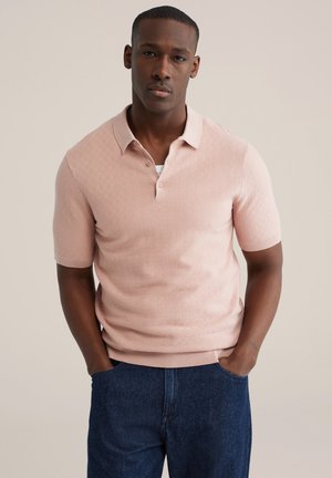 Lichtroze polo met korte mouwen en een gestructureerd patroon, knoopsluiting bij de kraag en geribbelde zoom, gecombineerd met donkerblauwe denim jeans.