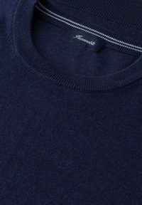 Zbliżenie na dekolt granatowego swetra z dzianiny z prążkowanym kołnierzem i metką z tkaniny wewnątrz szwu przy szyi.