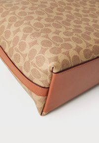 Borsa a mano in tessuto marrone a fantasia con base in pelle beige, caratterizzata da una forma strutturata e dettagli di cucitura in contrasto lungo i bordi.