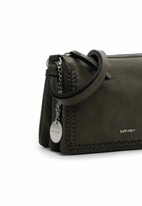 Borsa a mano in pelle verde oliva con dettagli intrecciati, catena argentata e etichetta metallica rotonda. Caratterizzata da una chiusura con zip e una tracolla regolabile.