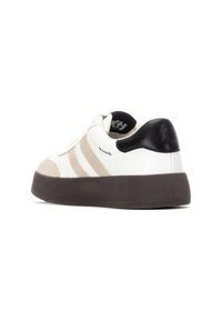 Zapatilla blanca con franjas beiges, talón negro, suela texturizada, puntera redonda y detalles cosidos. Materiales de cuero liso y gamuza.