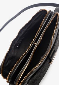 Black handbag featuring a textured exterior, two zippered compartments with gold-tone zippers, and a shoulder strap for easy carrying.