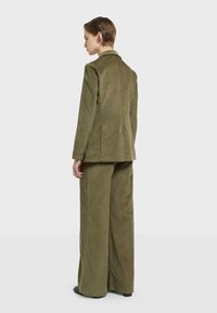 Olijfgroen corduroy pak met een getailleerde blazer met een metselkraag en wijde broekspijpen, textiel met verticale ribbels.
