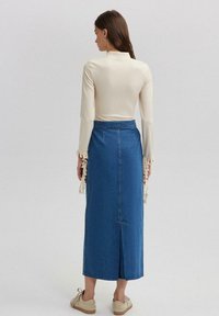 Lange mouw crèmekleurige top met franjes, gecombineerd met een mid-length blauwe denim rok met een achterkant split en een effen ontwerp.