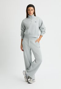 Sudadera corta de color gris claro con cuello de media cremallera y logotipo bordado, combinada con joggers de pierna ancha a juego con cordón.
