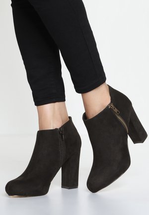 Bottines en daim noir avec un talon bloc haut et une fermeture éclair latérale, présentant un bout arrondi et une finition texturée.