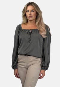 Szara bluzka z długim rękawem o kwadratowym dekolcie i detalach wiązania; zestawiona z beżowymi, dopasowanymi spodniami; gładka tekstura, luźna sylwetka.