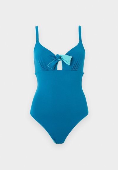 Μπλε ολόσωμο μαγιό με ρυθμιζόμενες τιράντες και λεπτομέρεια κόμπου στο μπροστινό μέρος πάνω από μια μικρή οπή.