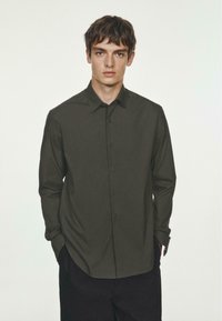 Dunkelgrünes Langarmhemd mit button-down Kragen, Frontknöpfen und geradem Saum. Hergestellt aus einem glatten Stoff ohne sichtbare Muster.