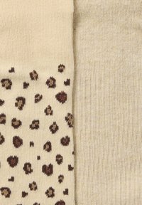 Leopardenmuster und einfarbige beige Crew-Socken. Weicher Strickstoff mit braunen und schwarzen Flecken auf einem Socken und einem feinen Rippenmuster auf dem anderen.