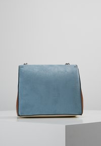 Modrá semišová obdélníková kabelka s hnědými akcenty, s hladkým povrchem a stříbrnými detaily. Má strukturovaný siluetu.