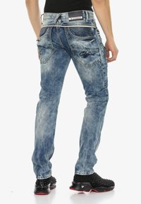 Verwaschene blaue Jeans mit geradem Bein, dekorativen Nähten, zwei Gesäßtaschen und einem Logo auf der linken Tasche.