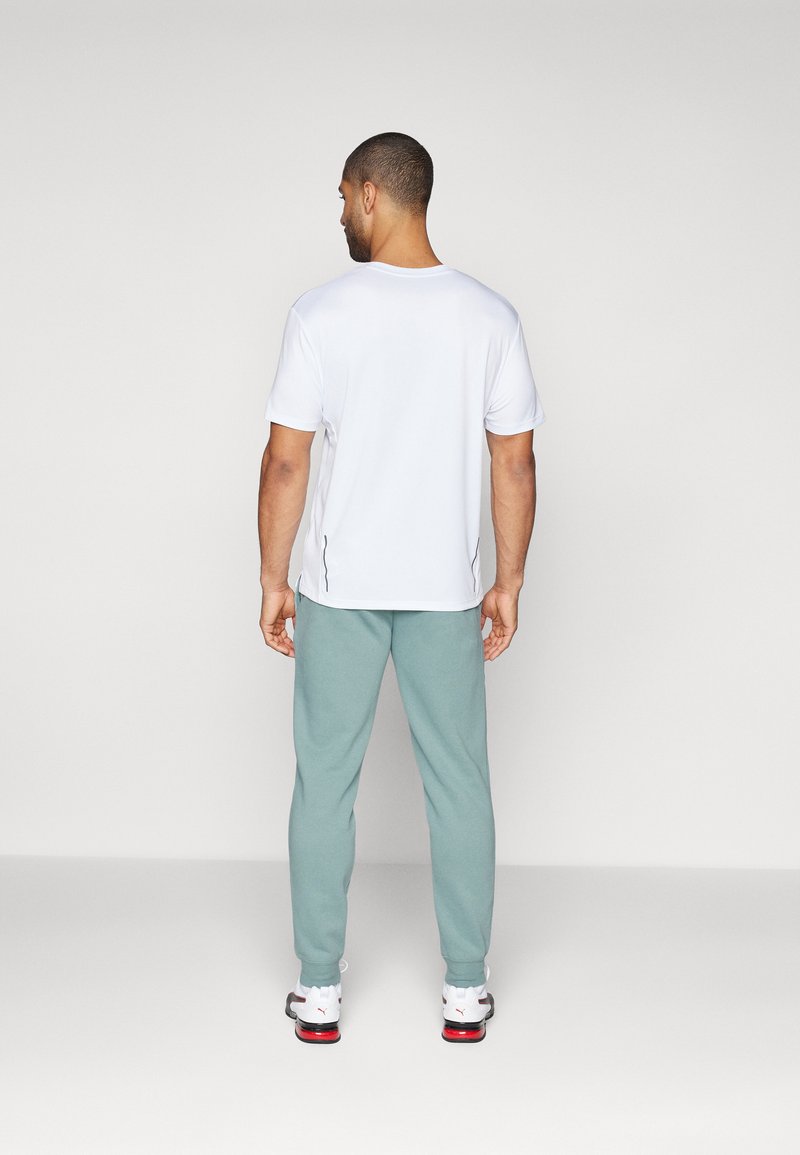 T-shirt bianca a maniche corte abbinata a pantaloni tuta verde chiaro. La t-shirt ha un semplice scollo rotondo; i pantaloni tuta sono larghi e morbidi.