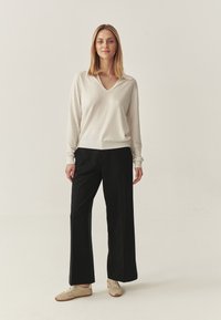 Pulover bej deschis cu decolteu în V, asortat cu pantaloni negri cu picioare late și adidași bej. Textură netedă; croială lejeră; design simplu.