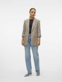 Beige blazer med skrå lapel, rullede ærmer og to forlommer, parret med en sort top og lyseblå jeans, afsluttet med blå hæle.