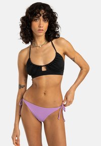 Black bikini top with ruching and a front keyhole detail, paired with lavender tie-side bikini bottoms. Smooth fabric and slim straps.